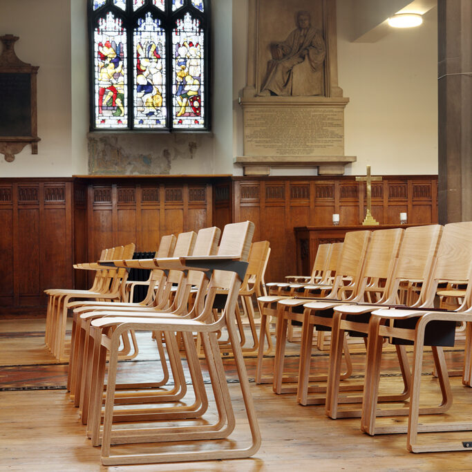 Wooden stacking chairs in a church with arms and book holders