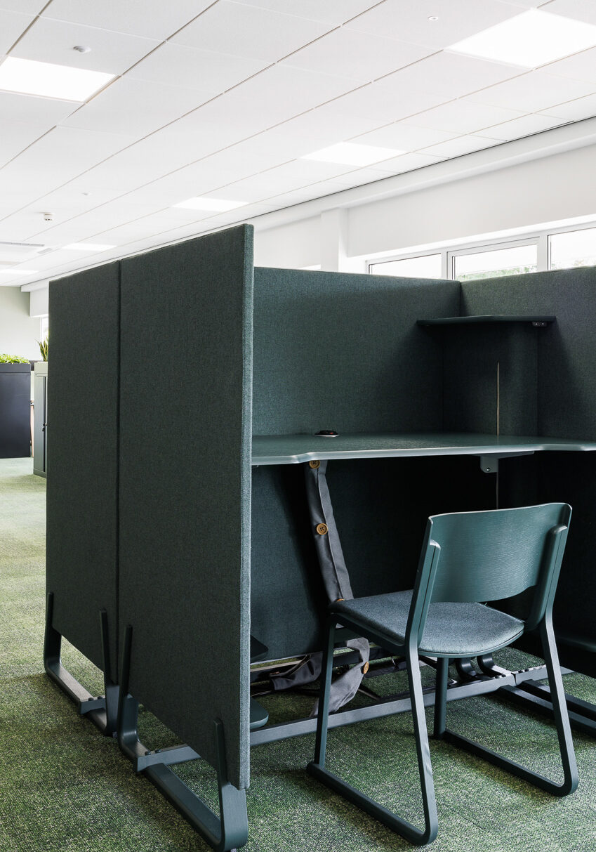 Two dark green free-standing office booths with adjustable standing or seated desk. Complete with cable management and matching green stacking chair.